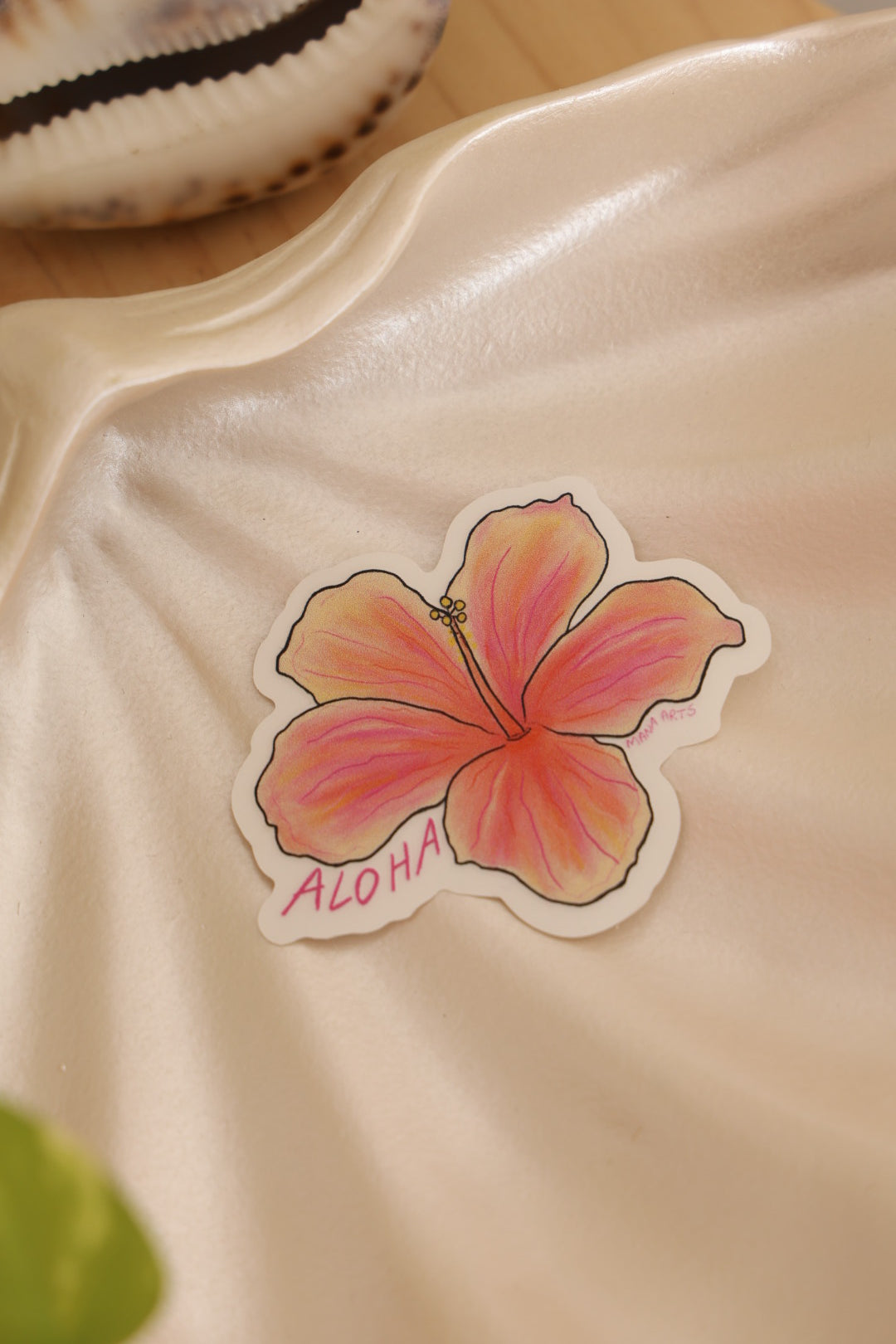 Sticker of a pink flower with 'ALOHA' text on a beige surface